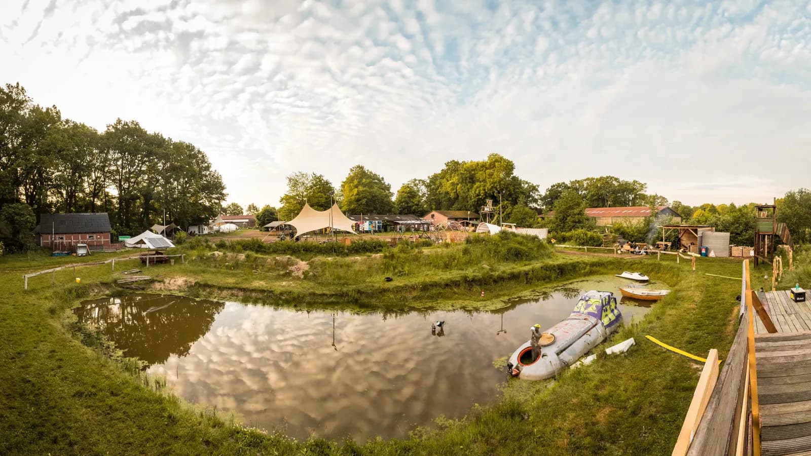 Zeltwiese mit Glampingzelten und Booten an einem Teich