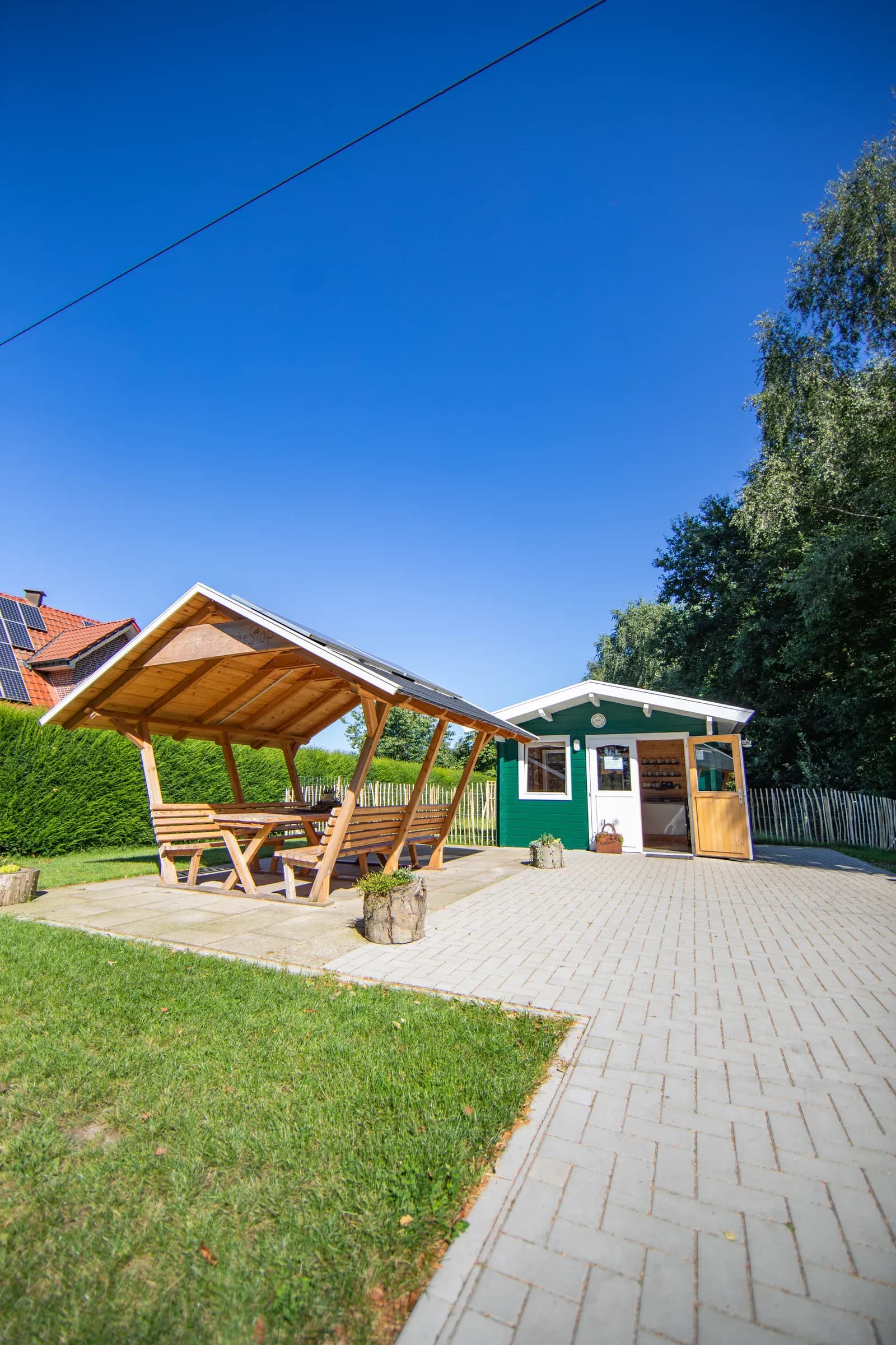 Holzhütte mit überdachter Sitzgruppe neben einer grünen Hecke
