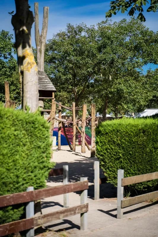 Spielplatz mit Kletterturm und Rutsche zwischen Hecken und Bäumen auf einem Campingplatz