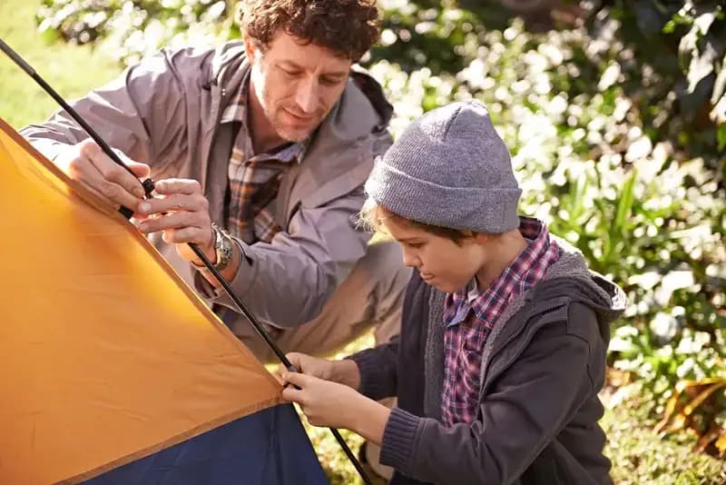 Vater und Sohn stecken gemeinsam die Stangen eines Zeltes zusammen