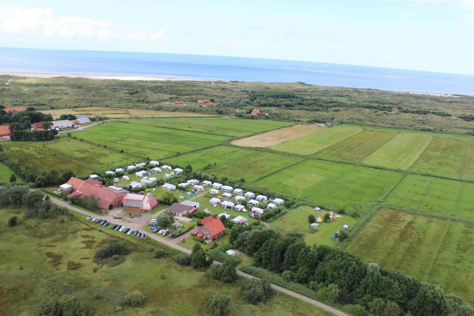 Luftbild eines Campingplatzes zwischen Feldern und Deich mit der Nordsee am Horizont