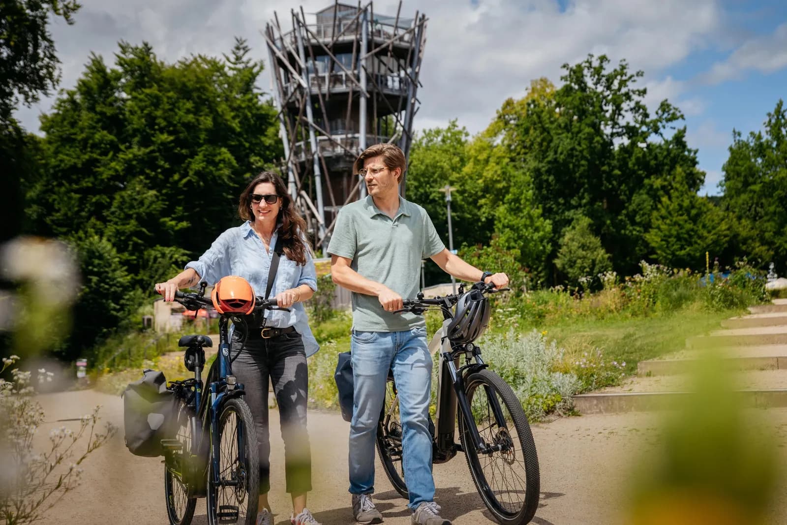 Zwei Menschen mit E-Bikes vor einem Aussichtsturm im Grünen