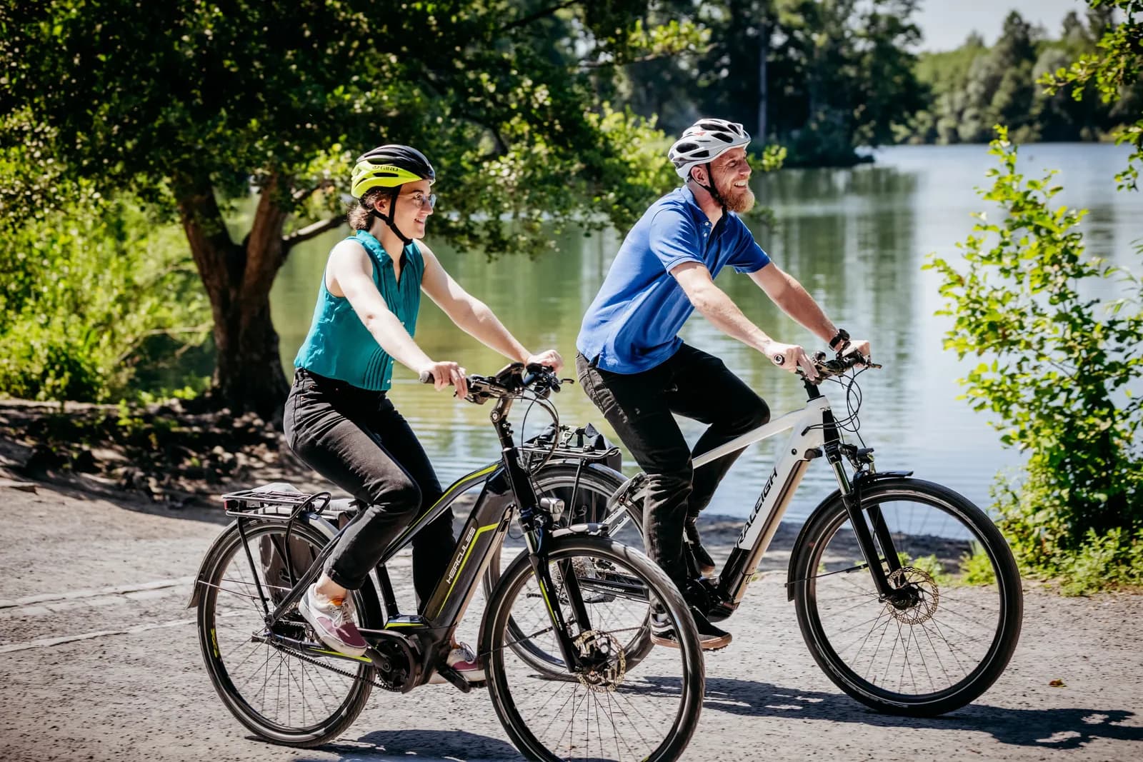 Zwei Radfahrende mit Helmen auf einem sonnigen Weg am See