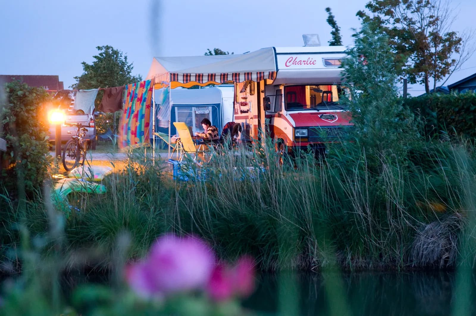 Wohnwagen mit Markise und Lichterkette am Abend, davor blühendes Gras