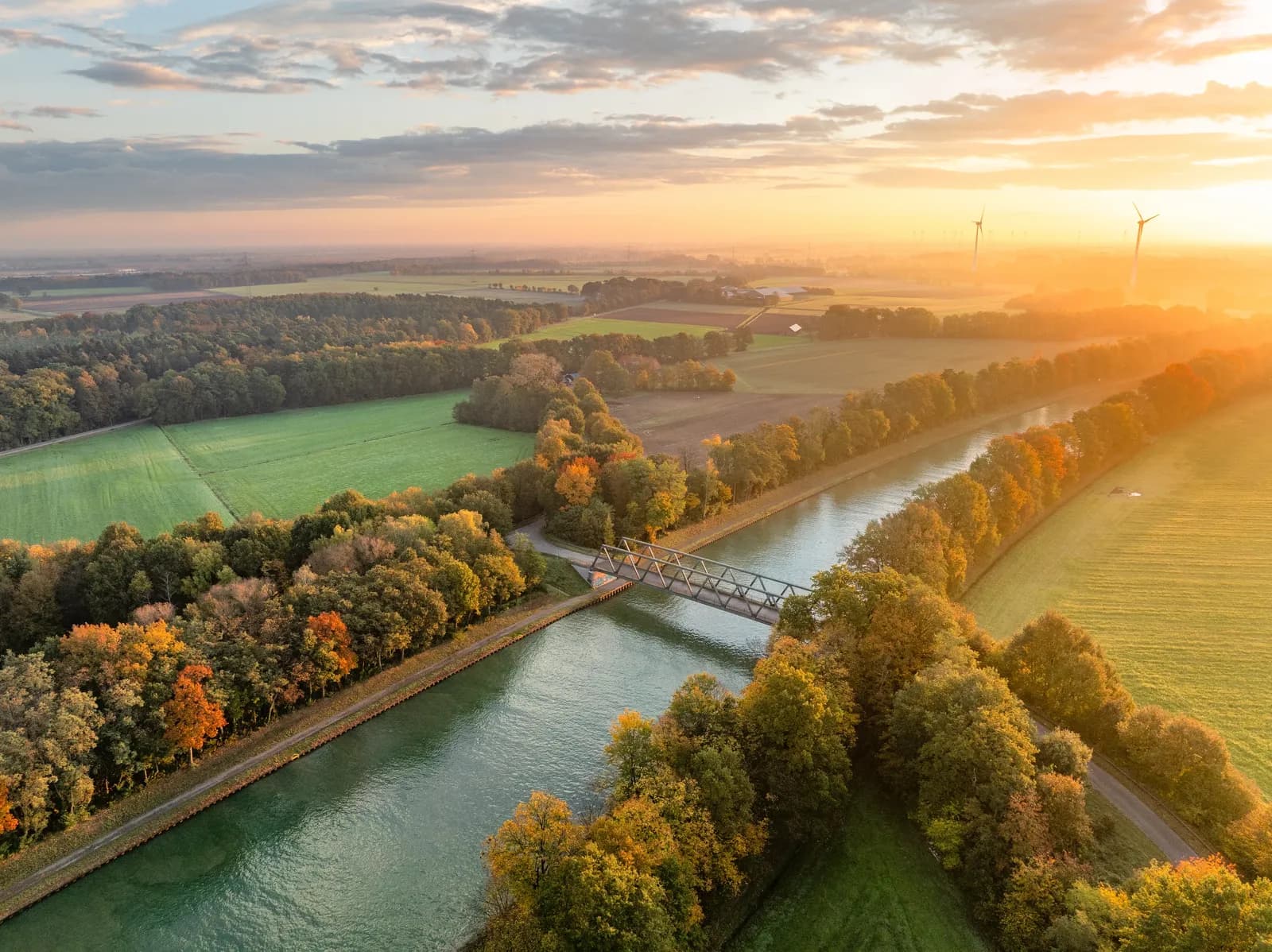 Luftbild eines Kanals mit Brücke zwischen herbstlich gefärbten Bäumen im Sonnenaufgang