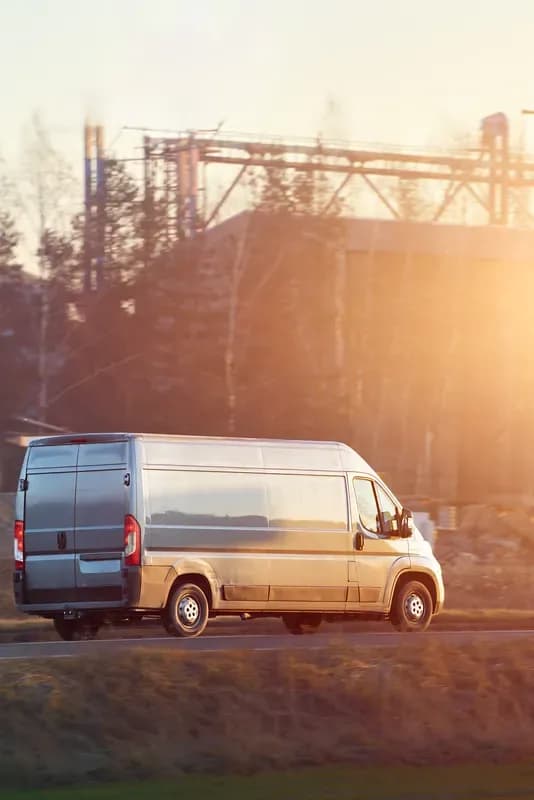 Weißer Kastenwagen auf einer Landstraße im Gegenlicht der tief stehenden Sonne